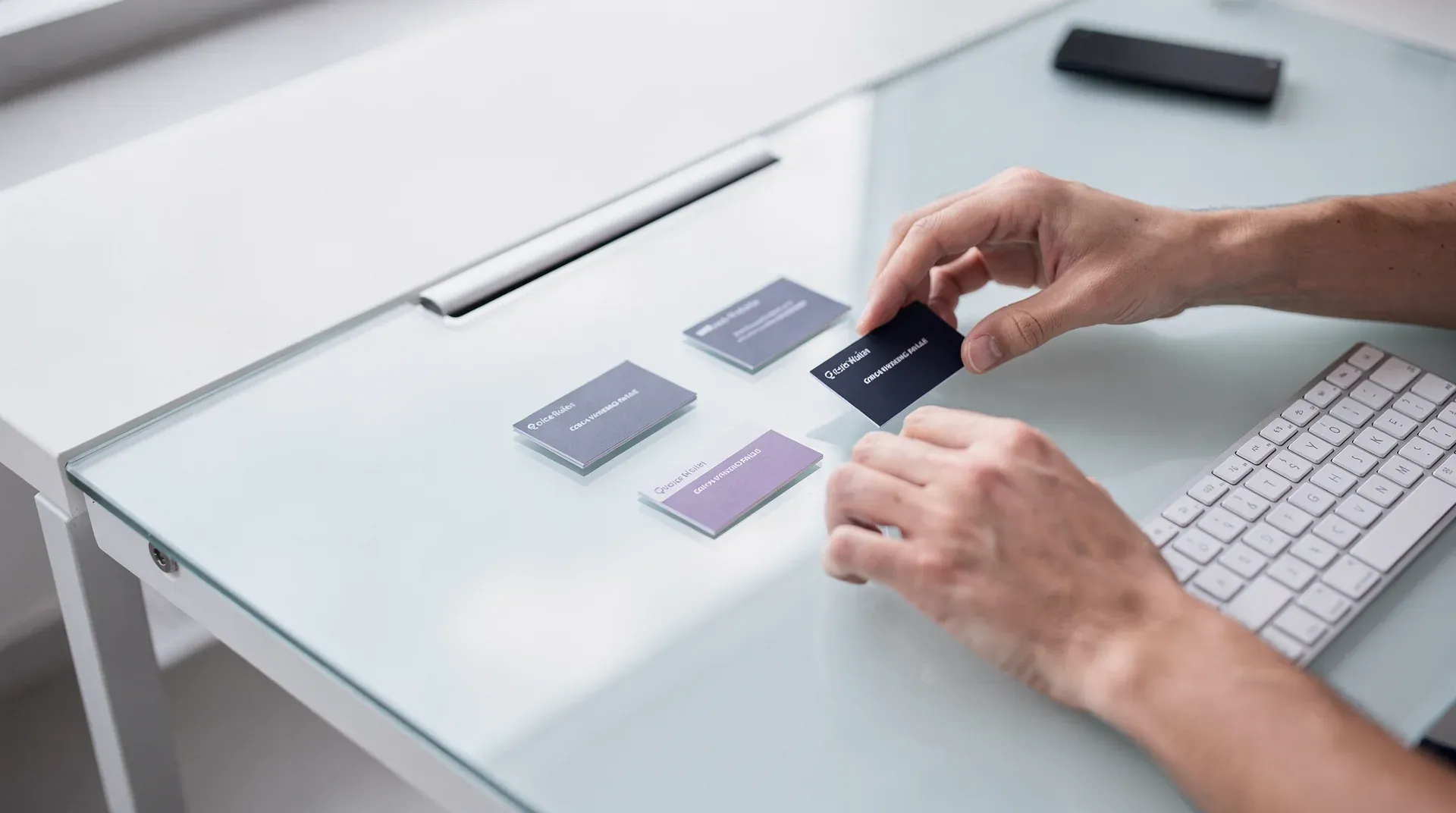 Hands arranging small white cards with faded labels on a bright desk, keyboard nearby